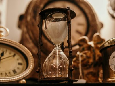 pexels-photo-1095601-1095601 Close-up of a vintage hourglass surrounded by antique clocks in warm lighting.